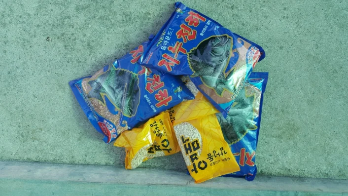 파란색 감성돔 집어제 봉투들과 노란색 압맥 봉투 두 개를 바닥에 모아 둔 모습